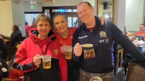 Francesca Murphy Francesca stands between her mother and father in the pub. They were all smiling and looking happy and holding pints of beer.