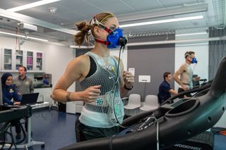 Photo of a woman wearing an oxygen mask and running on a treadmill while wearing a Samsung Galaxy Watch.