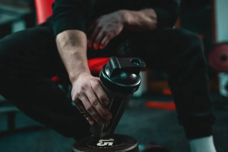 Close up of a person sitting down in the gym holding a black reusable water bottle.